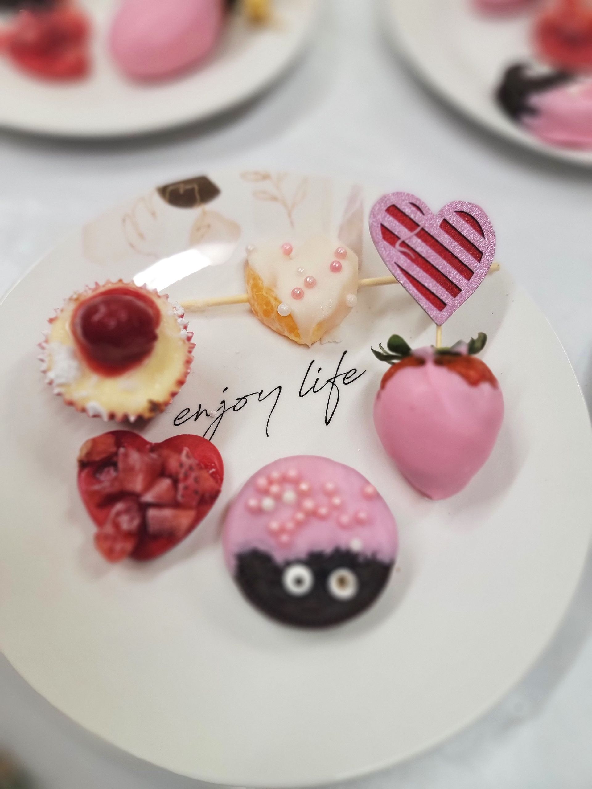 Dessert plate with various pink treats, including strawberries, heart-shaped candies, and a cupcake.