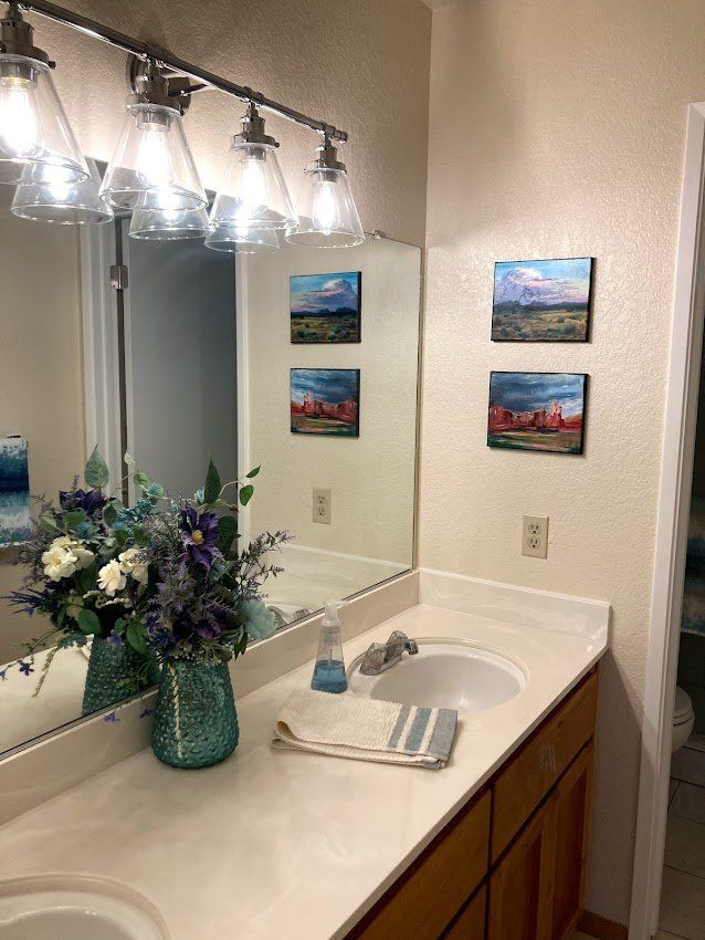 Bathroom with artwork above the sink. Blue and white flowers, a mirror, and light fixtures.