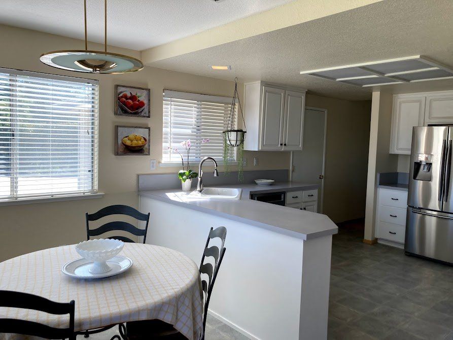 Kitchen with round table, countertop, white cabinets, and stainless steel refrigerator.