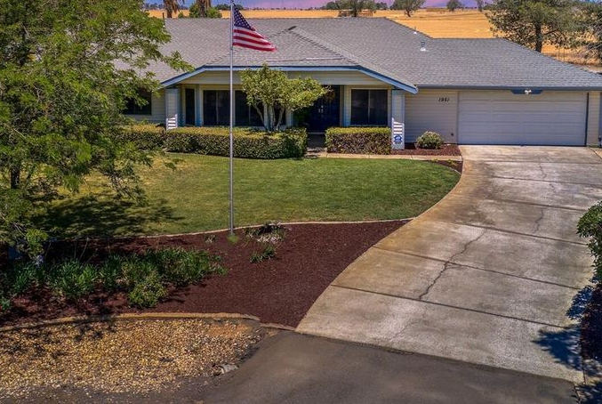House with American flag, green lawn, and long driveway. Sunny day.