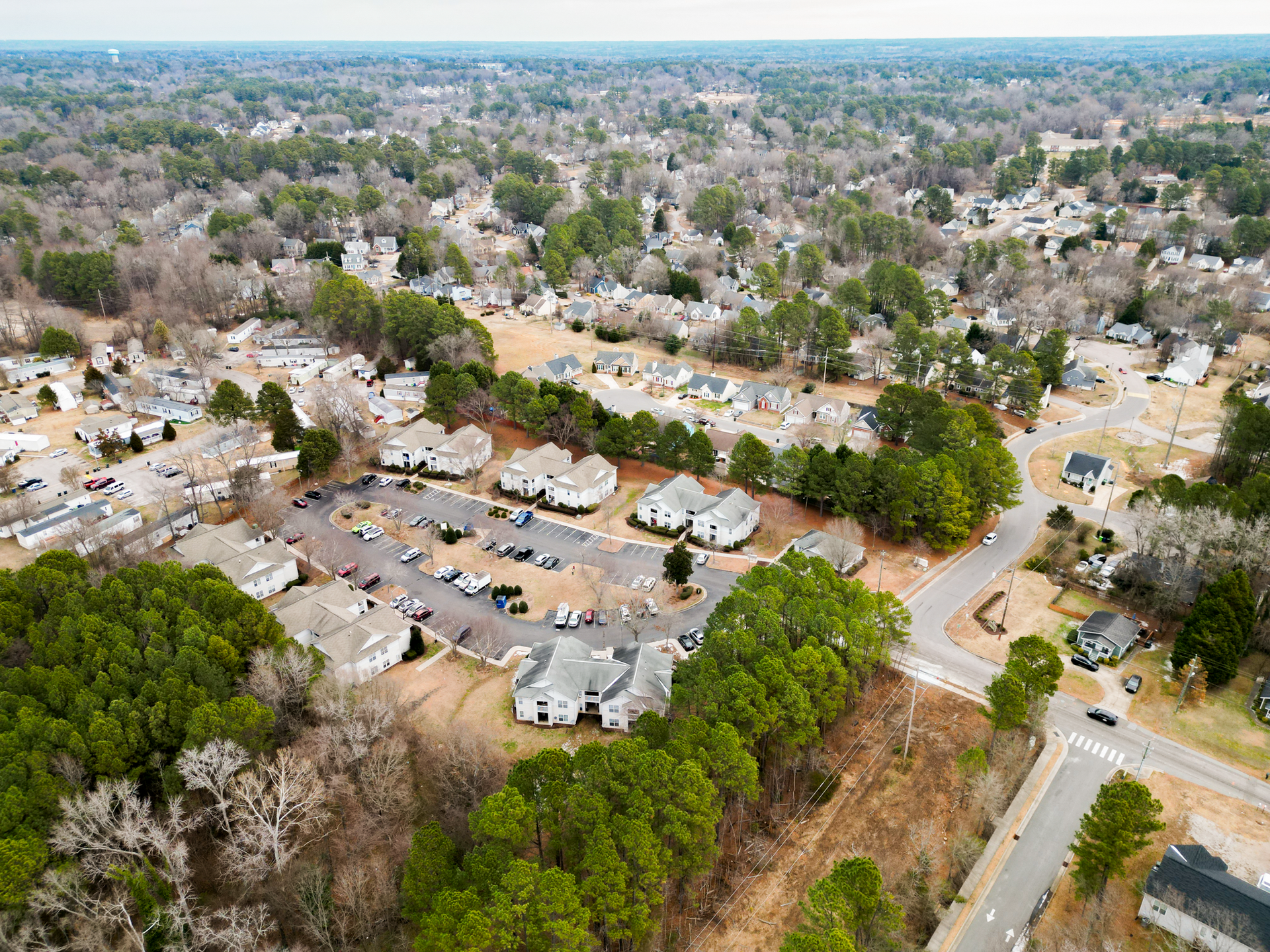 Aerial view of a suburban neighborhood with trees, houses, and parked cars.