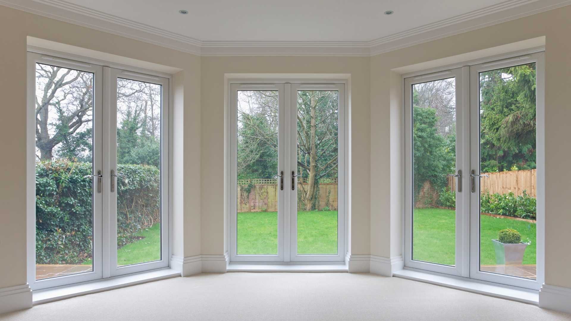 White French doors in a light-colored room open to a backyard with green lawn and trees.