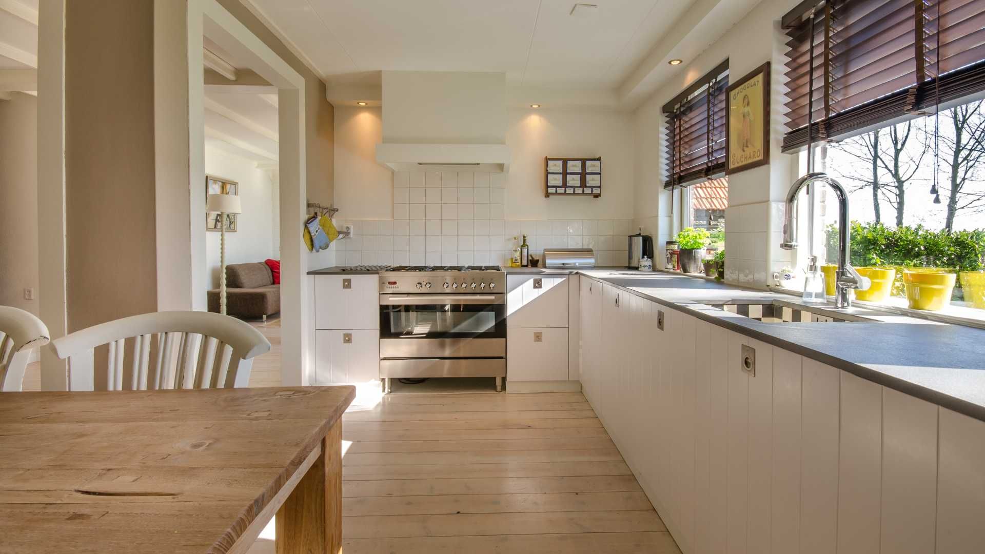 Light-filled kitchen with white cabinets, stainless steel appliances, and a wooden table. Sunlight streams through the window.