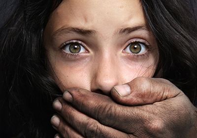 A close-up shot of a person with wide, expressive eyes having their mouth covered by a large, weathered, and dirty hand.