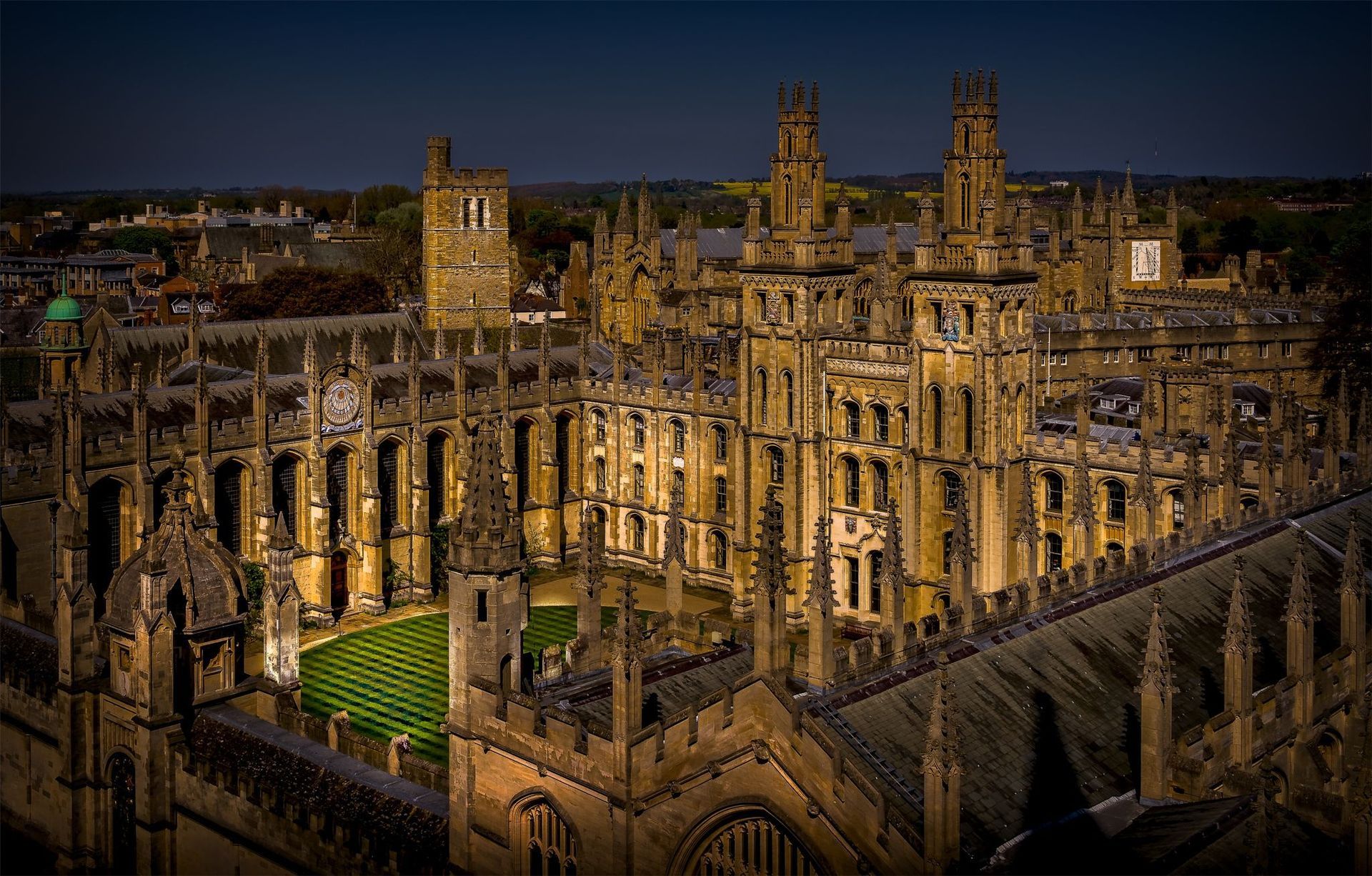 Aerial view of the Radcliffe Camera in Oxford, England, at dusk, surrounded by historic stone buildings and lit walkways.