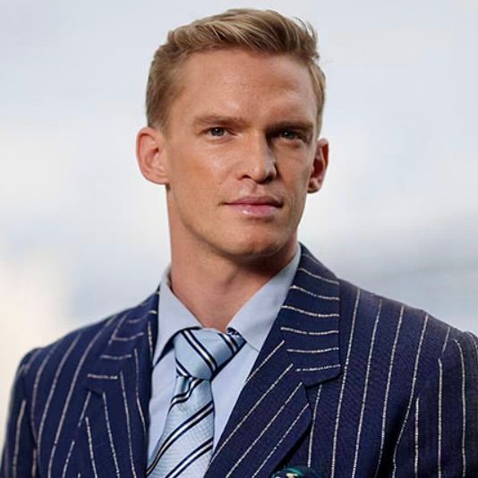 A person in a blue pinstripe suit, light blue collared shirt, and matching striped tie poses against a blurred background.