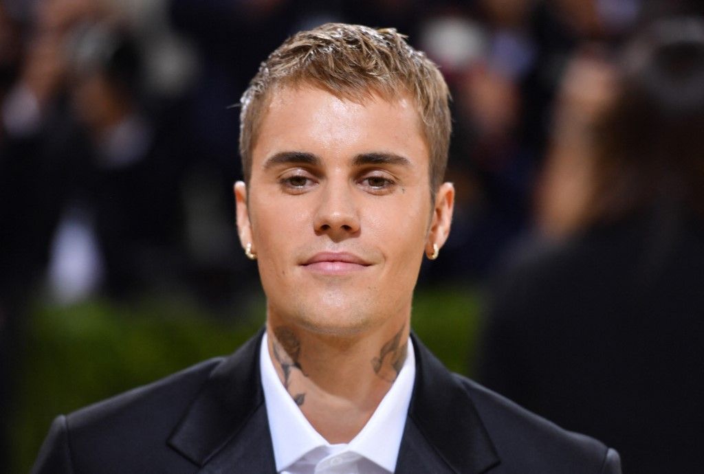 Justin Bieber wearing a black suit and white shirt, looking forward with a neutral expression at a formal event.