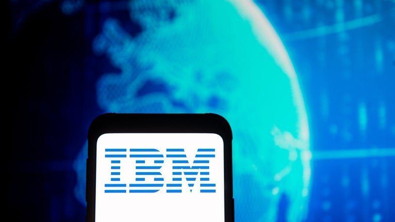 A smartphone screen displays the blue-striped IBM logo against a background of a glowing digital globe.