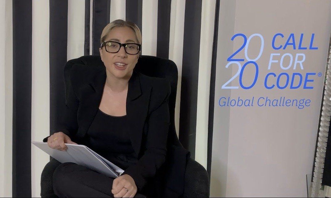 Lady Gaga wearing glasses sits in a black chair against a striped backdrop, next to a 2020 Call for Code text overlay.
