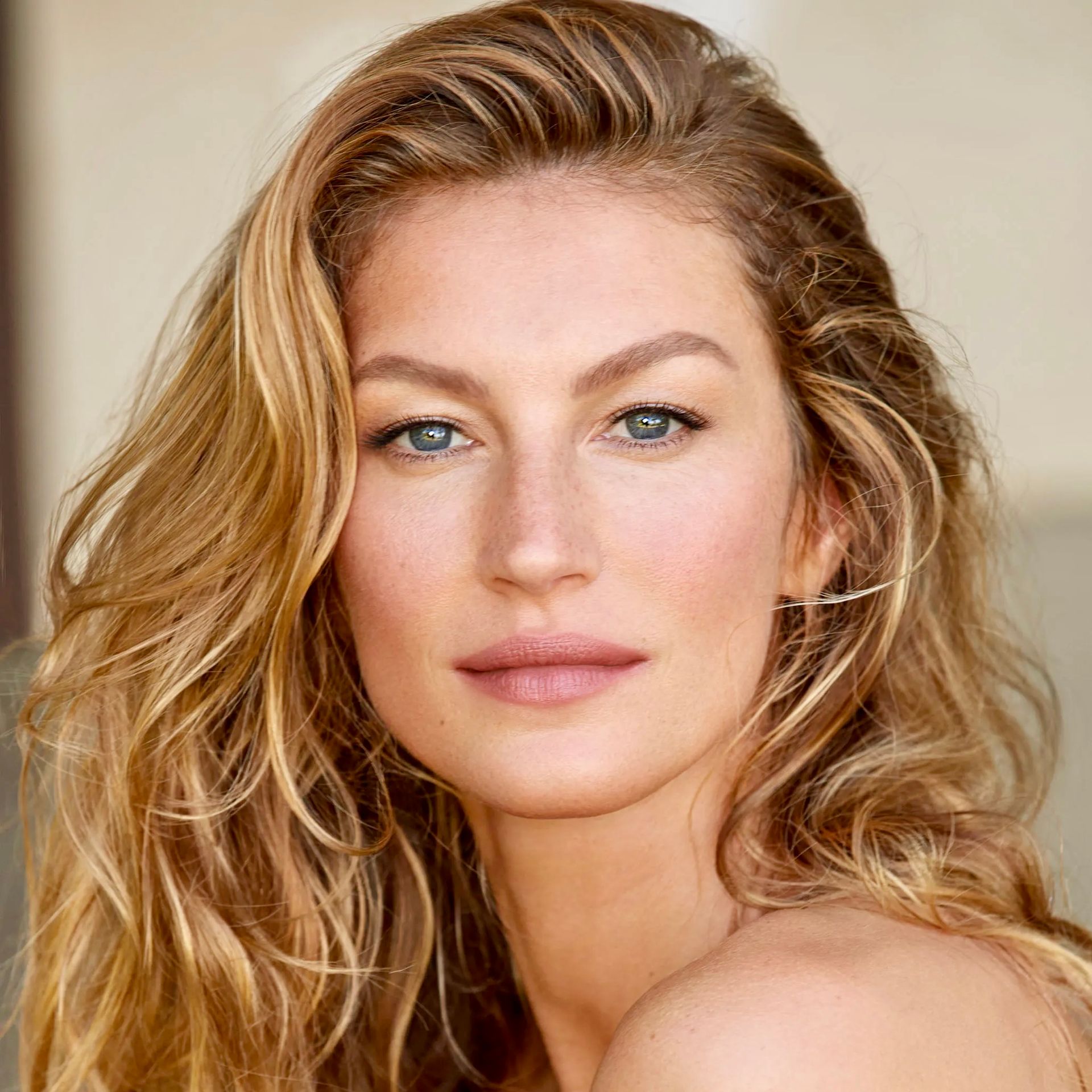 Portrait of Gisele Bündchen with long wavy blonde hair and a neutral expression against a light background.