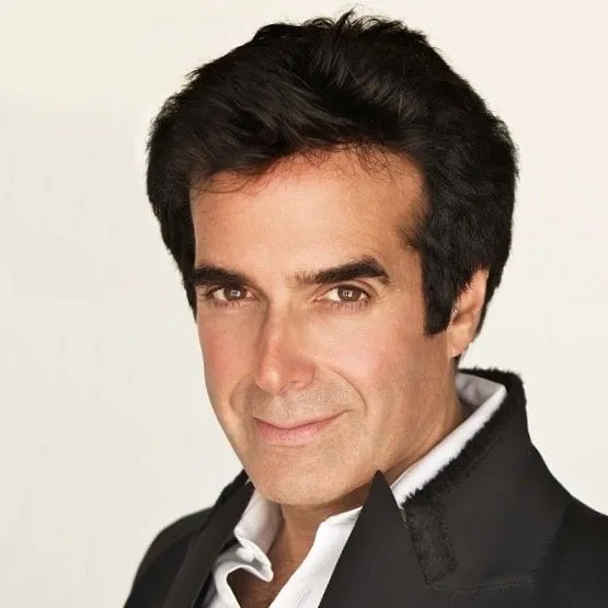 A close-up portrait of David Copperfield against a white background, wearing a black blazer over a white collared shirt.