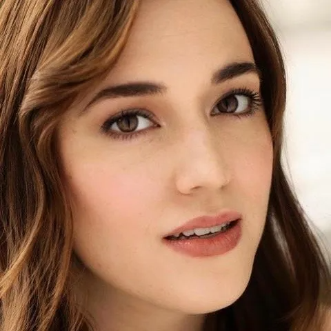 A close-up portrait of a person with wavy brown hair, looking directly at the camera with a neutral expression.