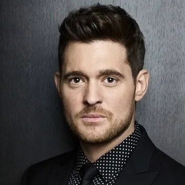 A studio headshot of Michael Bublé looking at the camera, wearing a black suit and a black-and-white polka-dot shirt.