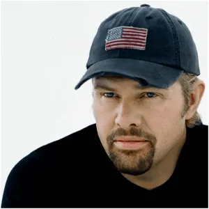 Close-up portrait of a person with a goatee wearing a dark blue baseball cap with an American flag patch.