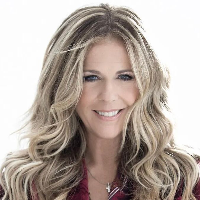 A woman with long, wavy blonde highlights smiling against a bright white background.