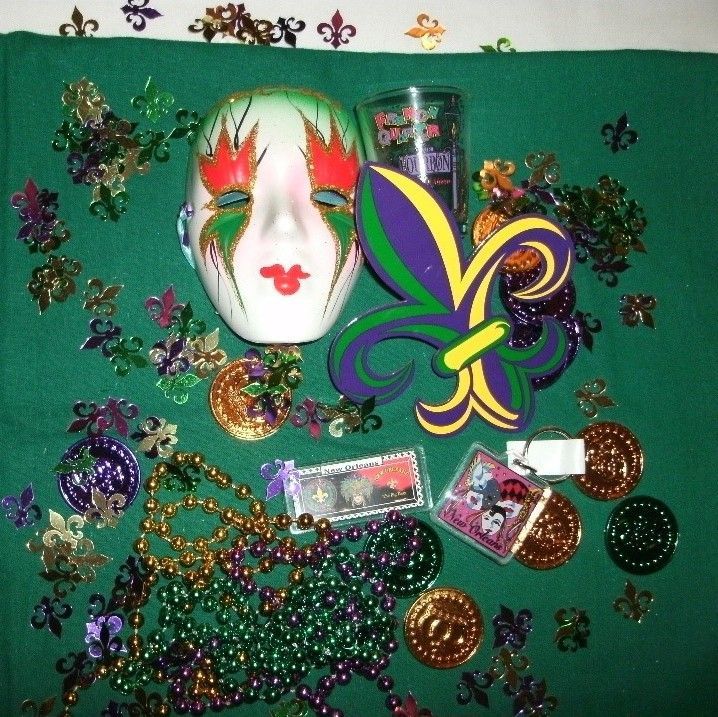 Mardi Gras display with a mask, fleur-de-lis, beads, coins, and shot glass on a green surface.