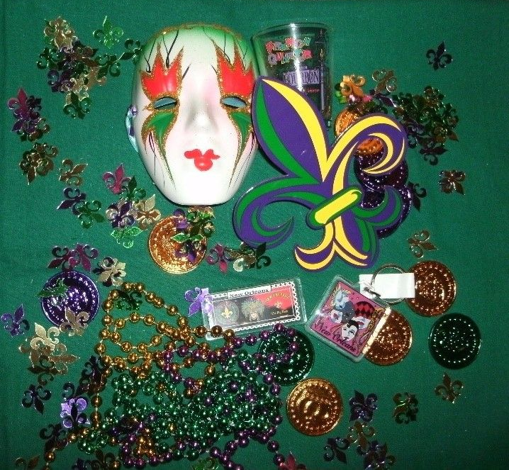 Mardi Gras display with a mask, fleur-de-lis, beads, coins, and shot glass on a green surface.