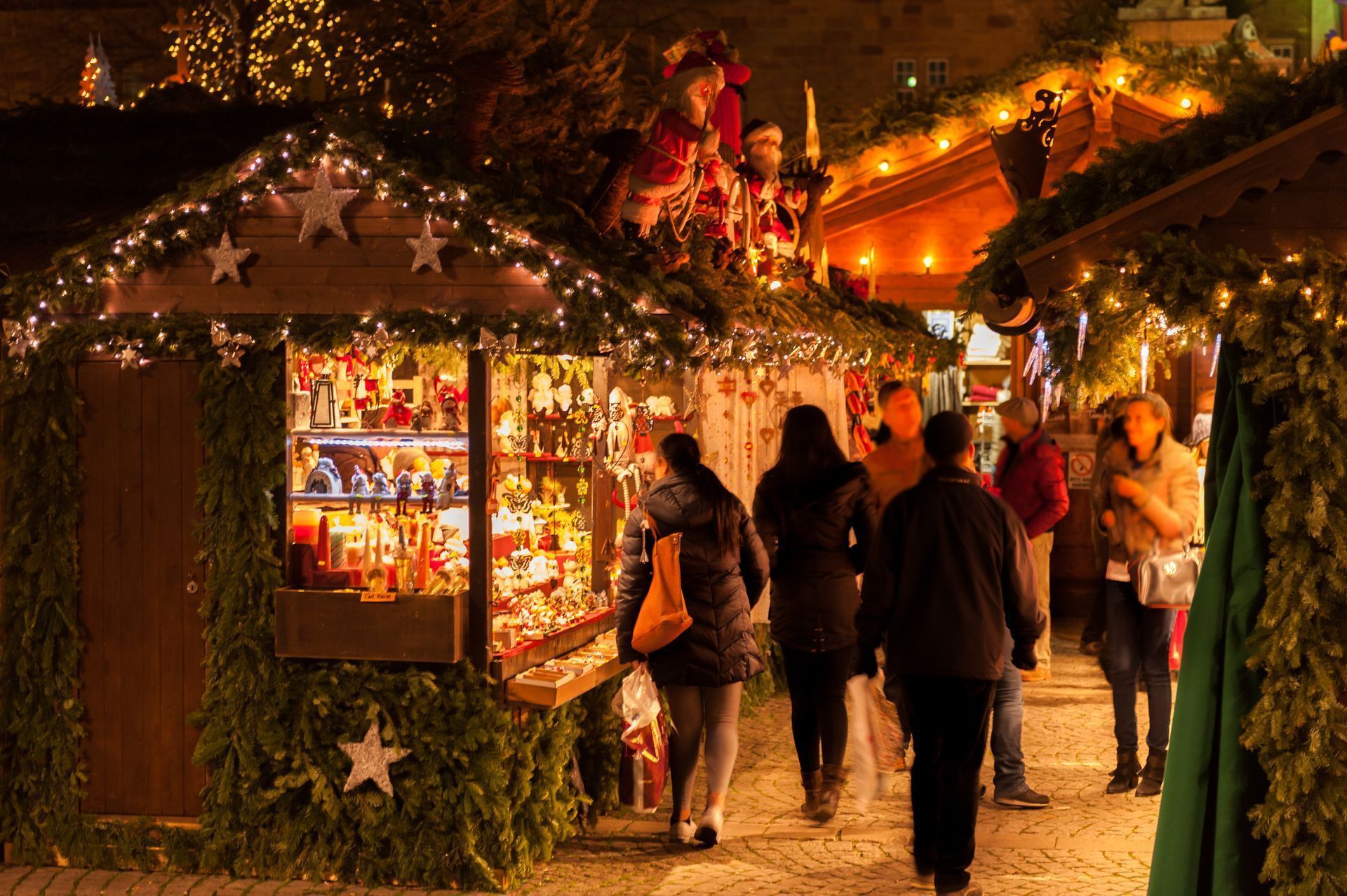 Christmas Market - People stroll through a festive holiday market adorned with lights and decorations, while some browse the stalls filled with various items for sale.