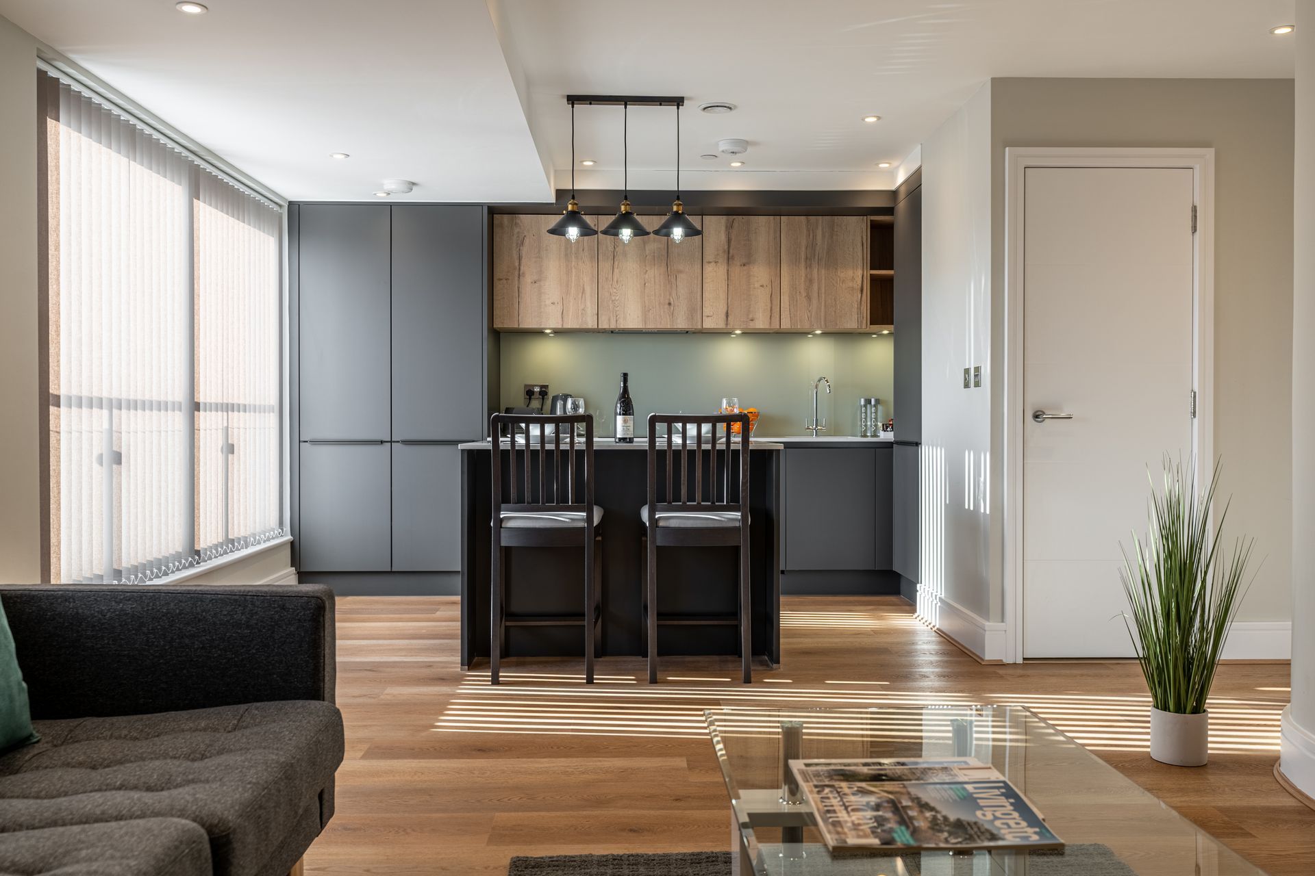 Modern kitchen with island, bar stools, pendant lights, and minimal decor in open living space.