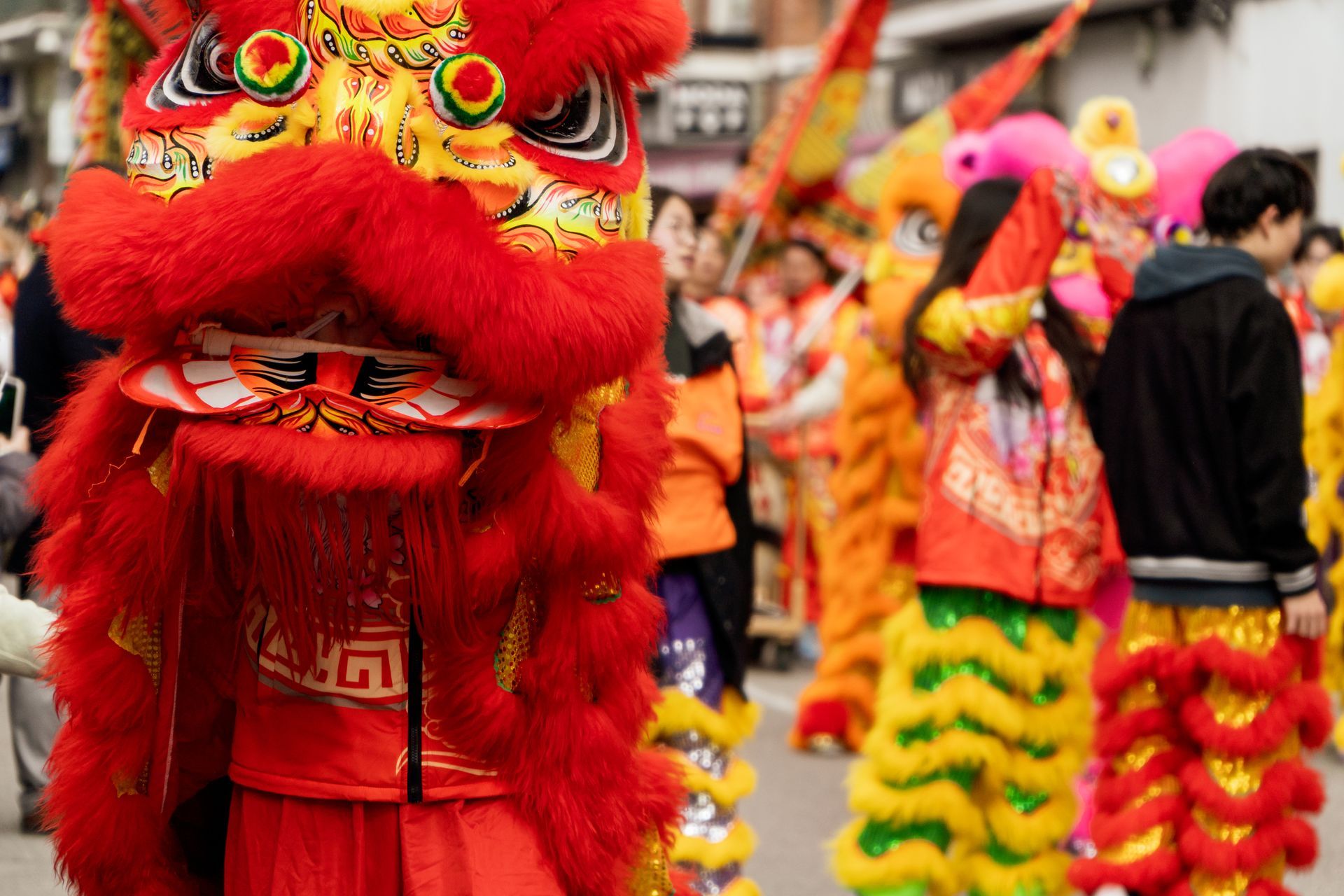 Performers in bright red and yellow lion costumes dance vibrantly in a Chinese New Year street parade in Reading, while excited onlookers cheer them on from the background.