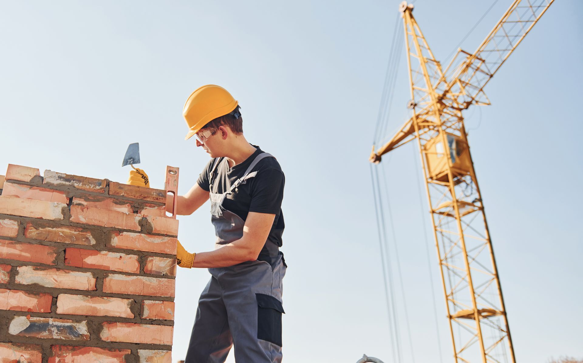 a man is working on a brick wall with a crane in the background