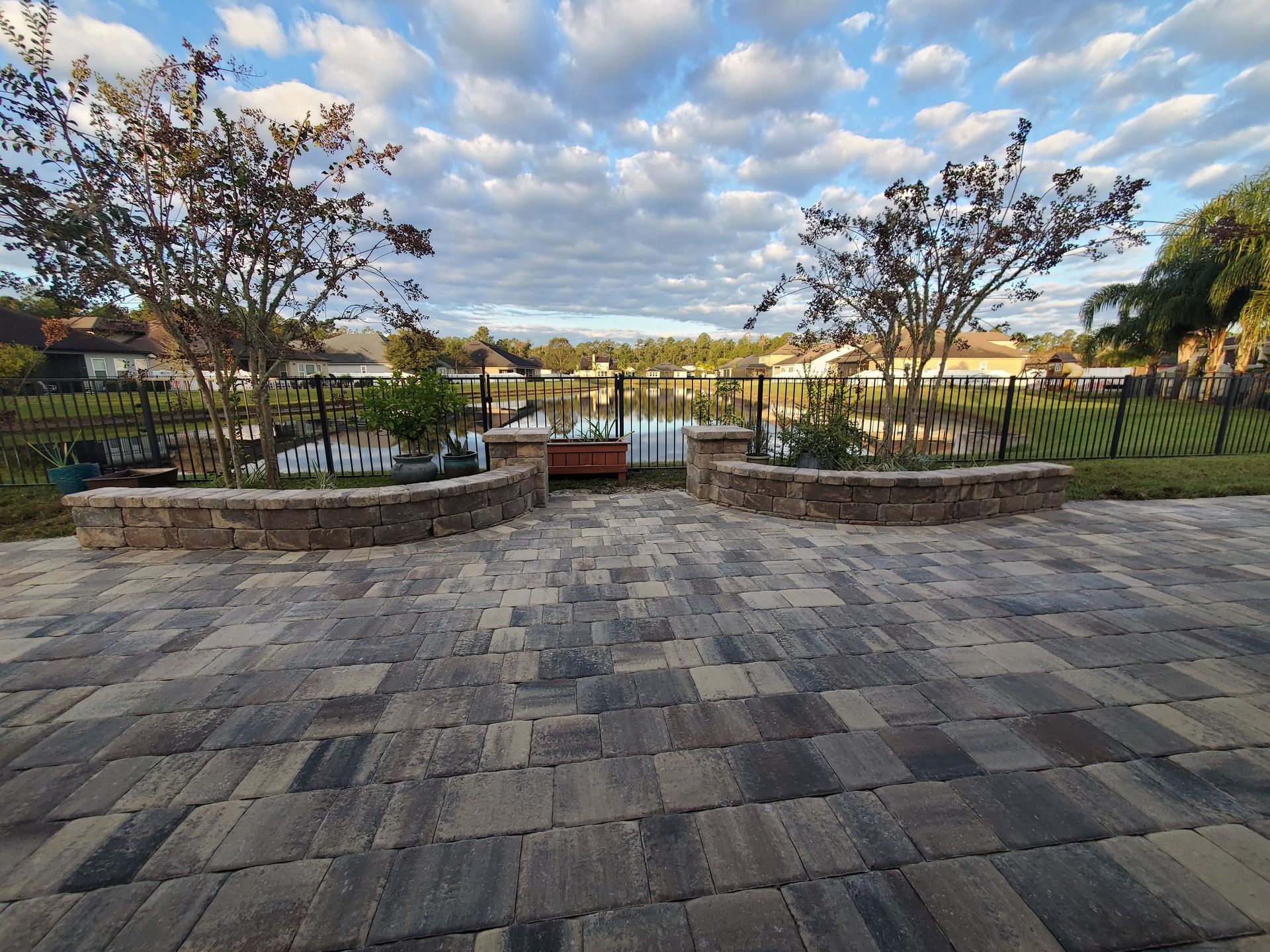 A brick patio with a fence and trees in the background.