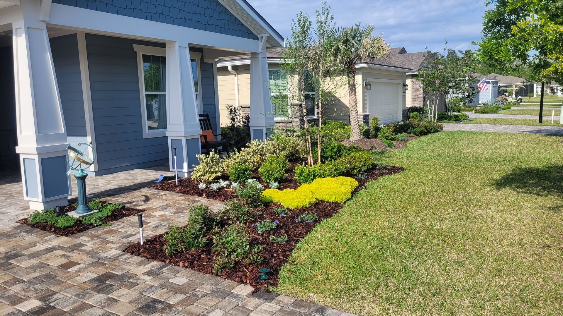 A blue house with a white porch and a garden in front of it.