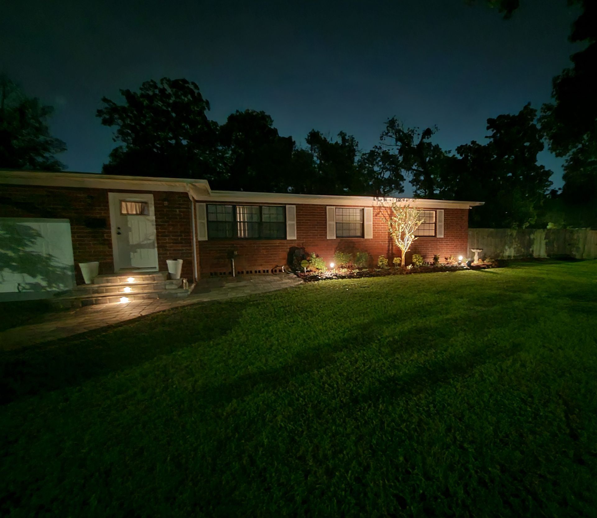 A brick house with a large lawn is lit up at night.