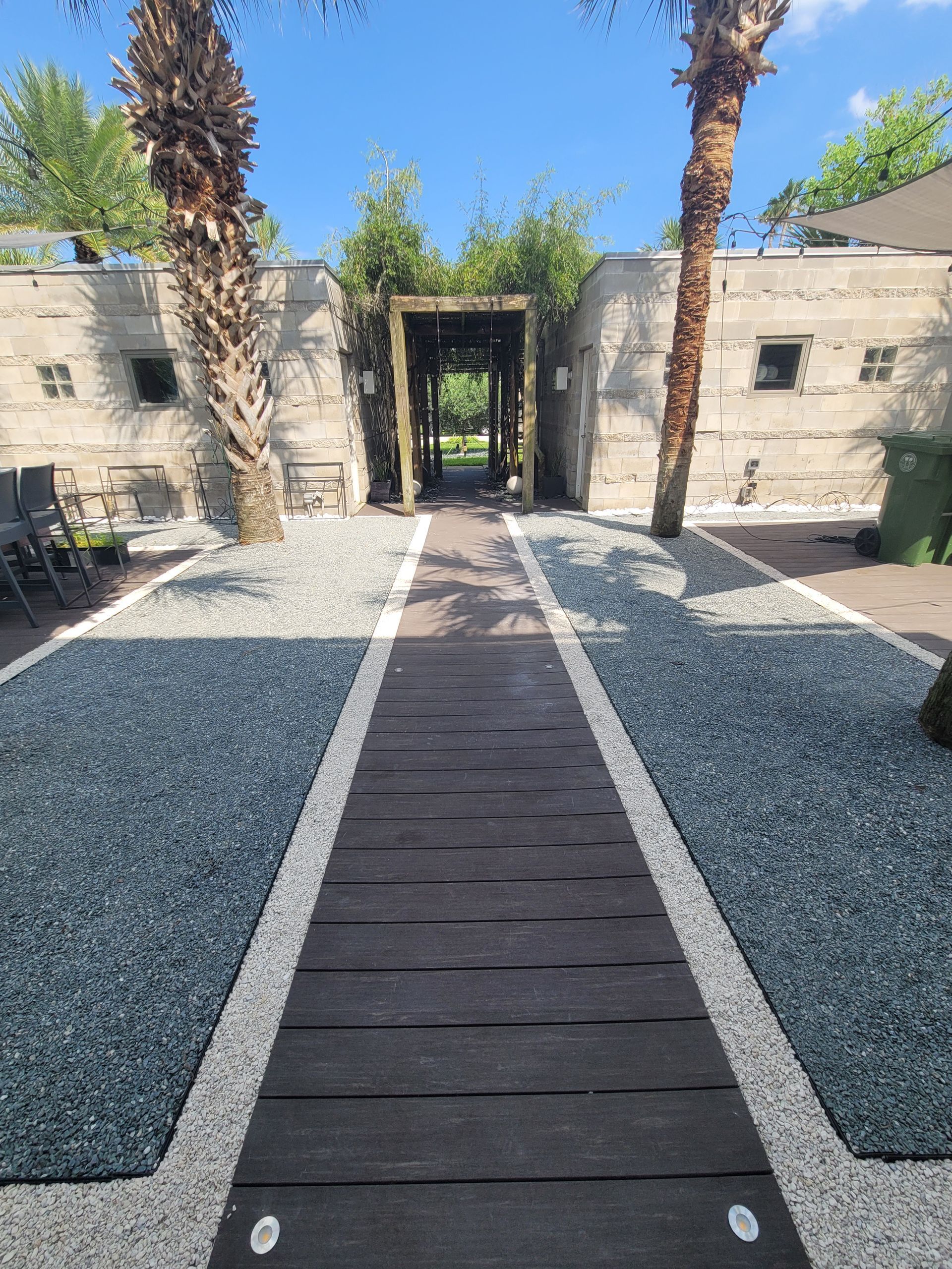 A walkway leading to a building with palm trees and gravel.