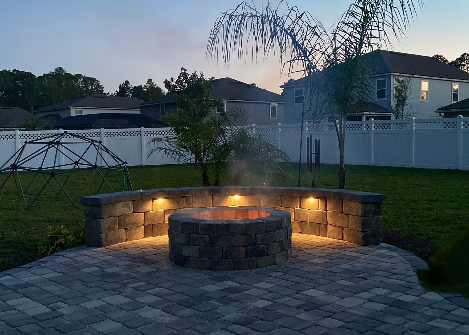 A fire pit is lit up at night in a backyard.