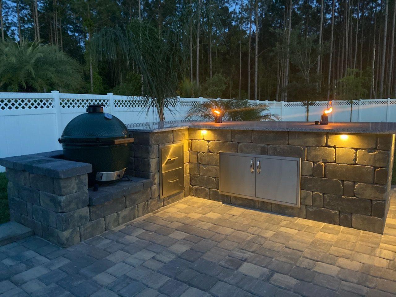 An outdoor kitchen with a green egg grill and a stainless steel cabinet.