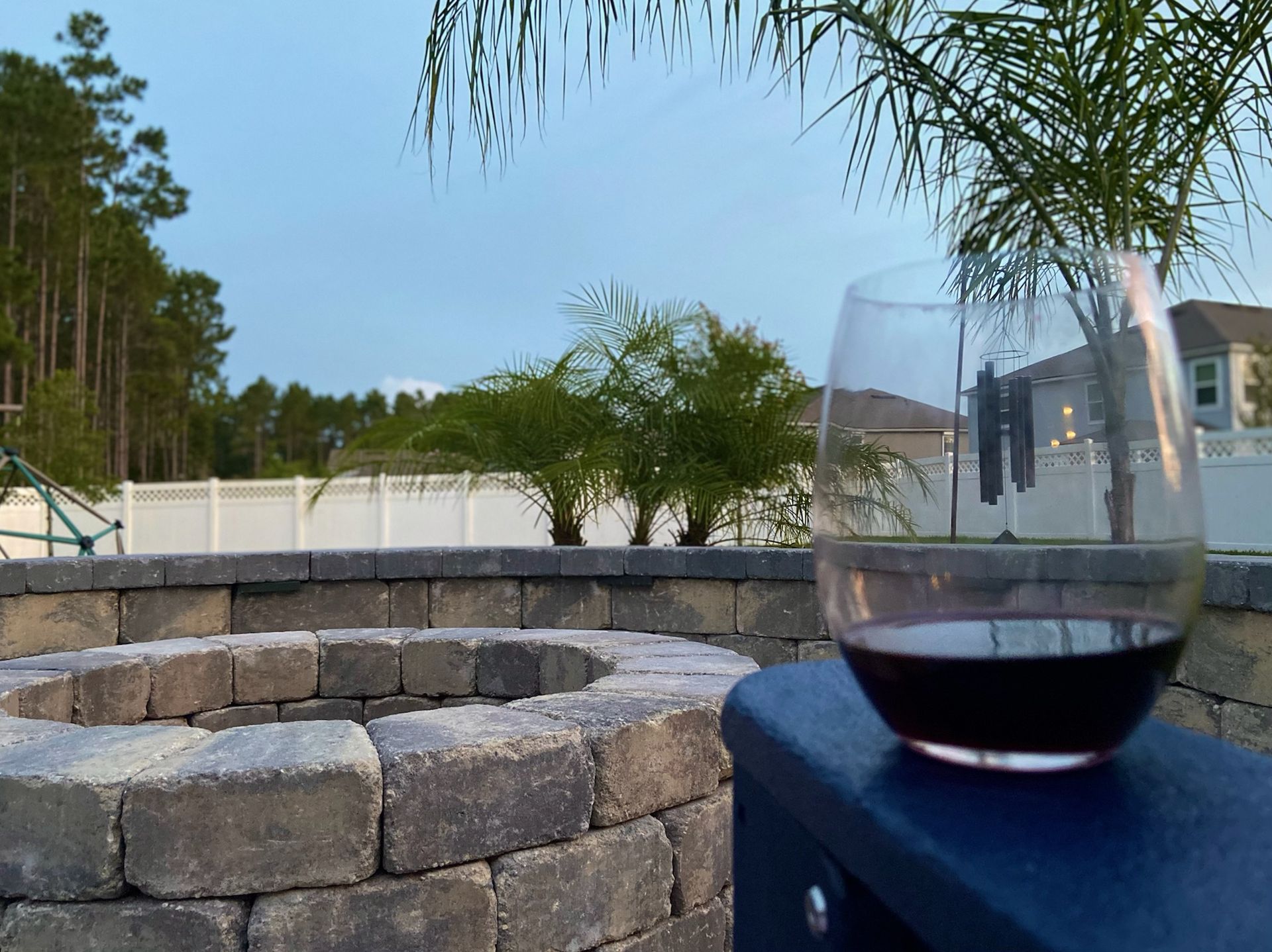 A glass of wine is sitting on a blue table next to a fire pit.