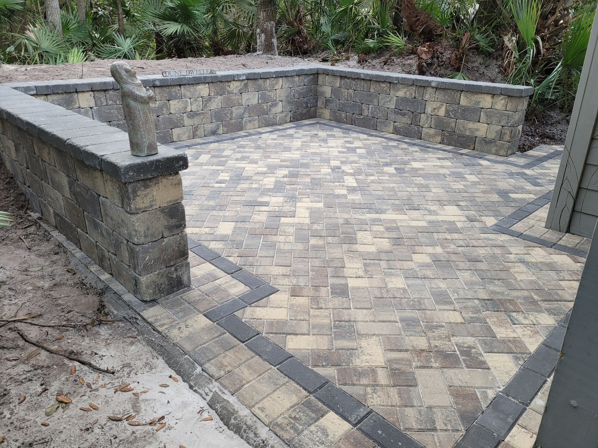 A brick patio with a stone wall and a bench.