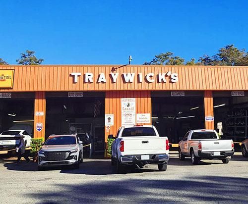 A car repair shop called Traywick's with trucks and a car parked out front on a sunny day.