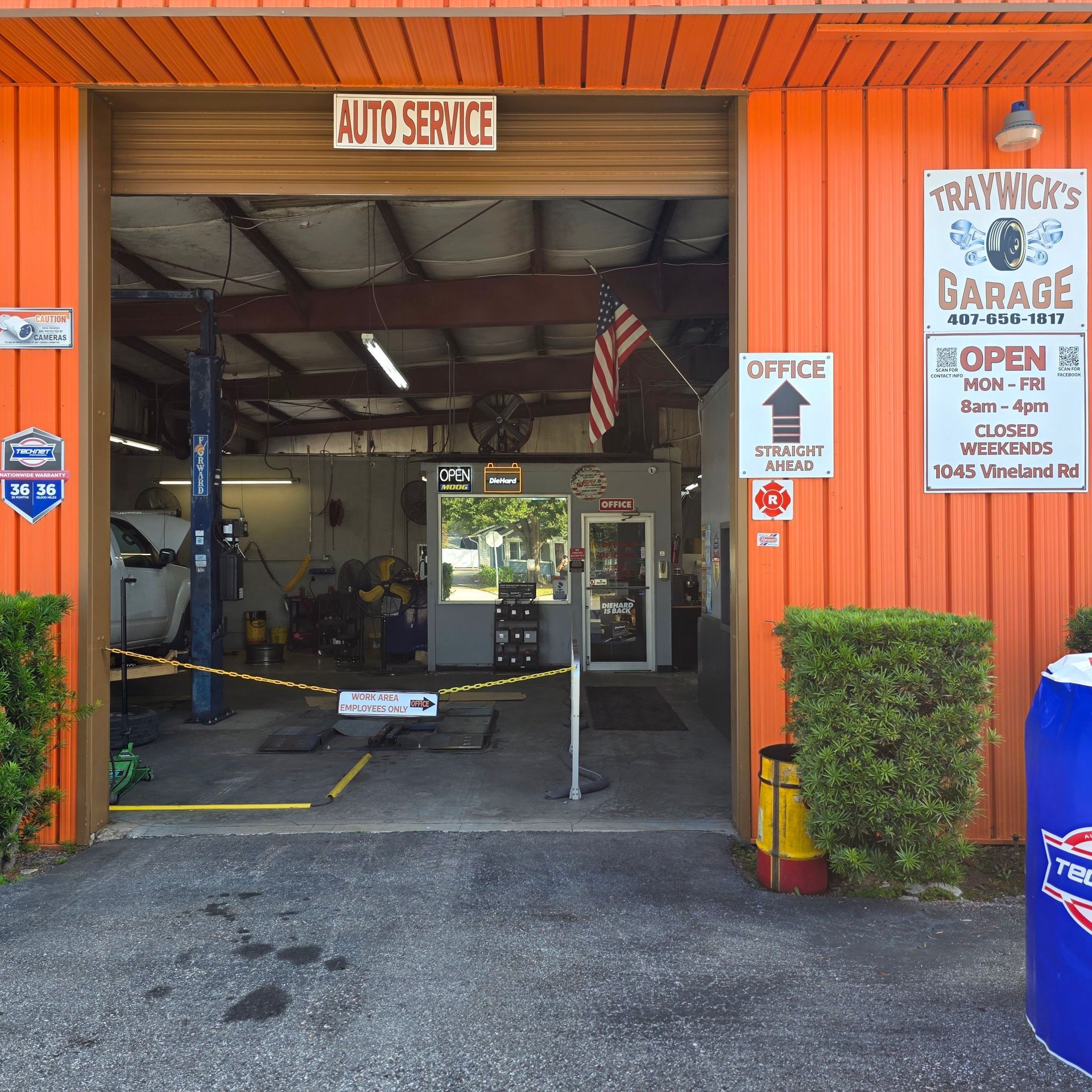 Exterior of Traywick's Garage auto shop with open bay door. Orange building with signs, tools, and a car lift visible inside.