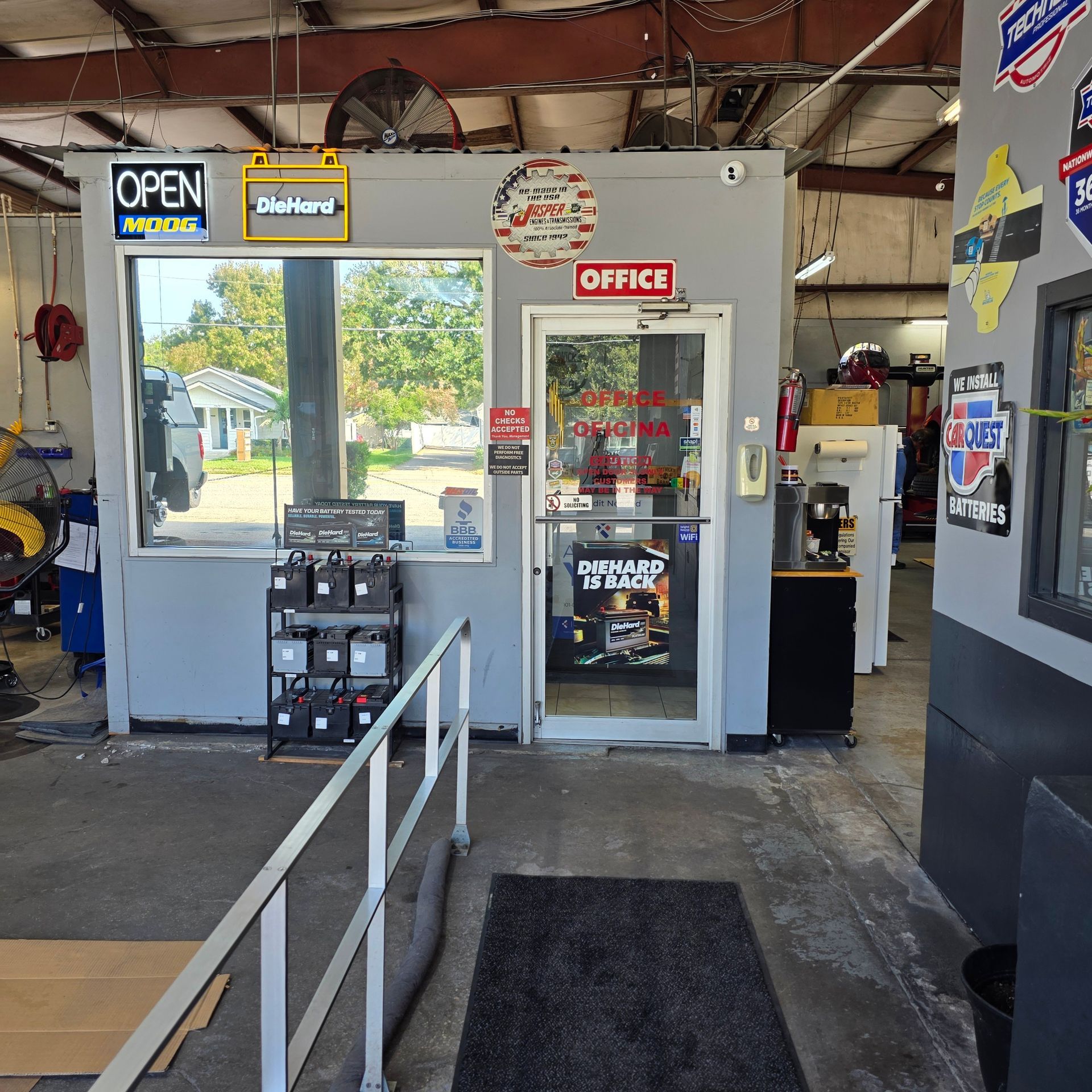 Entrance to a small auto repair shop; open sign, office door, batteries on display, and a ramp.