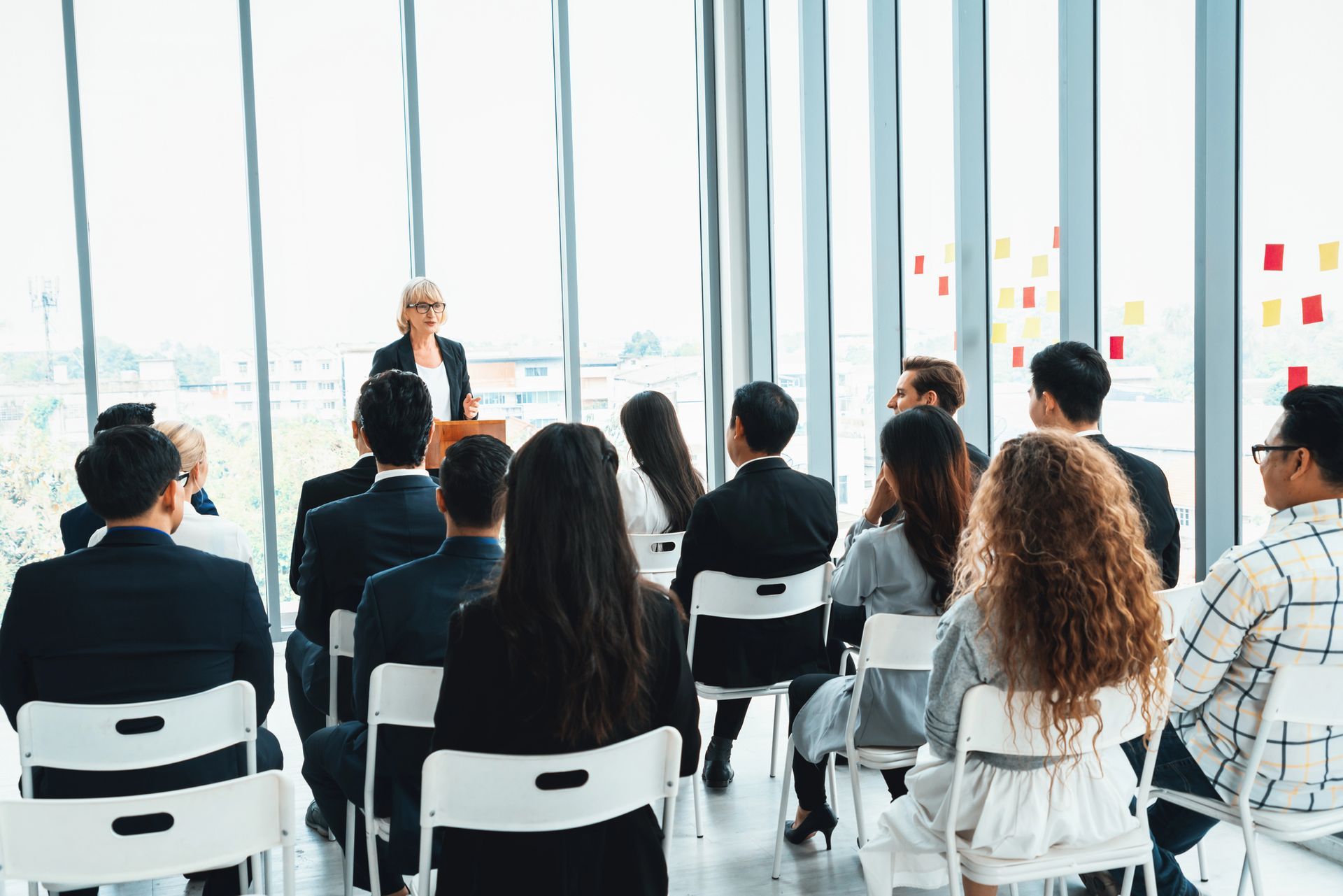 Un relatore si rivolge a un pubblico seduto in un ufficio moderno con ampie finestre.