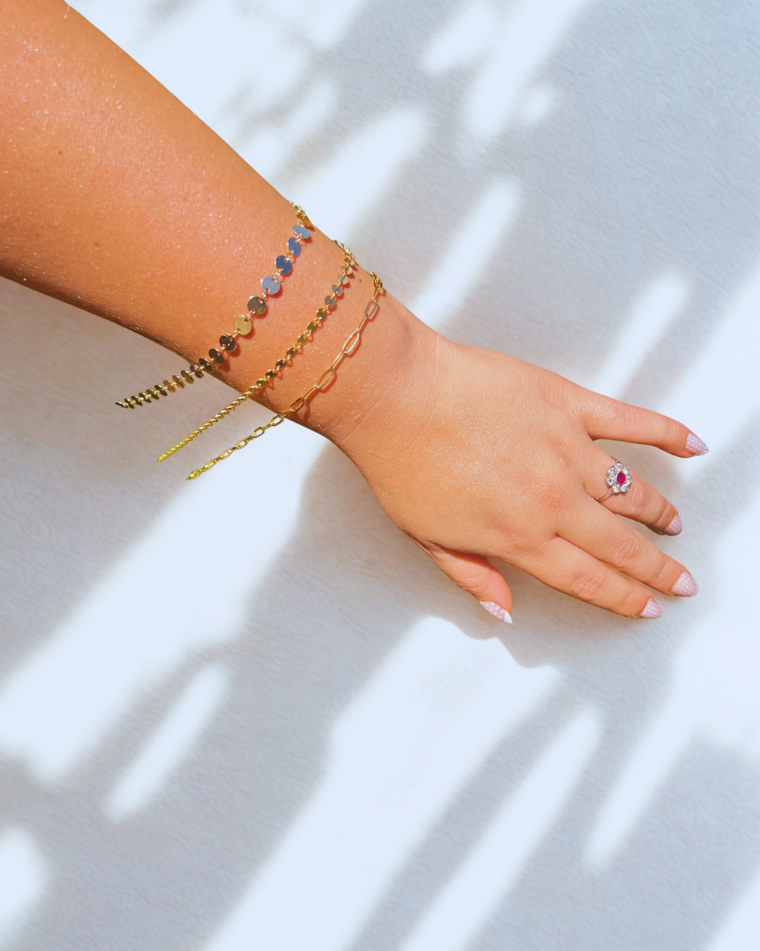 Arm with gold bracelets and a pink ring on a white surface with shadow.