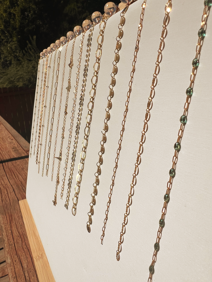 Gold necklaces hanging on a white display, with a natural wood background.