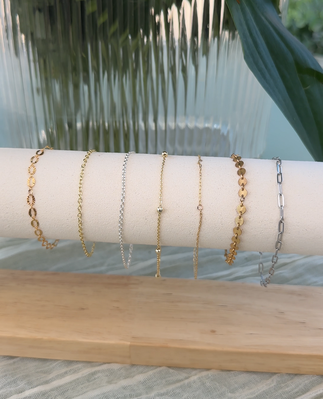 Seven delicate gold and silver chain bracelets displayed on a white fabric-covered roll.