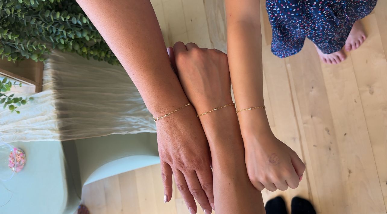 Three arms with matching gold bead bracelets clasped together.