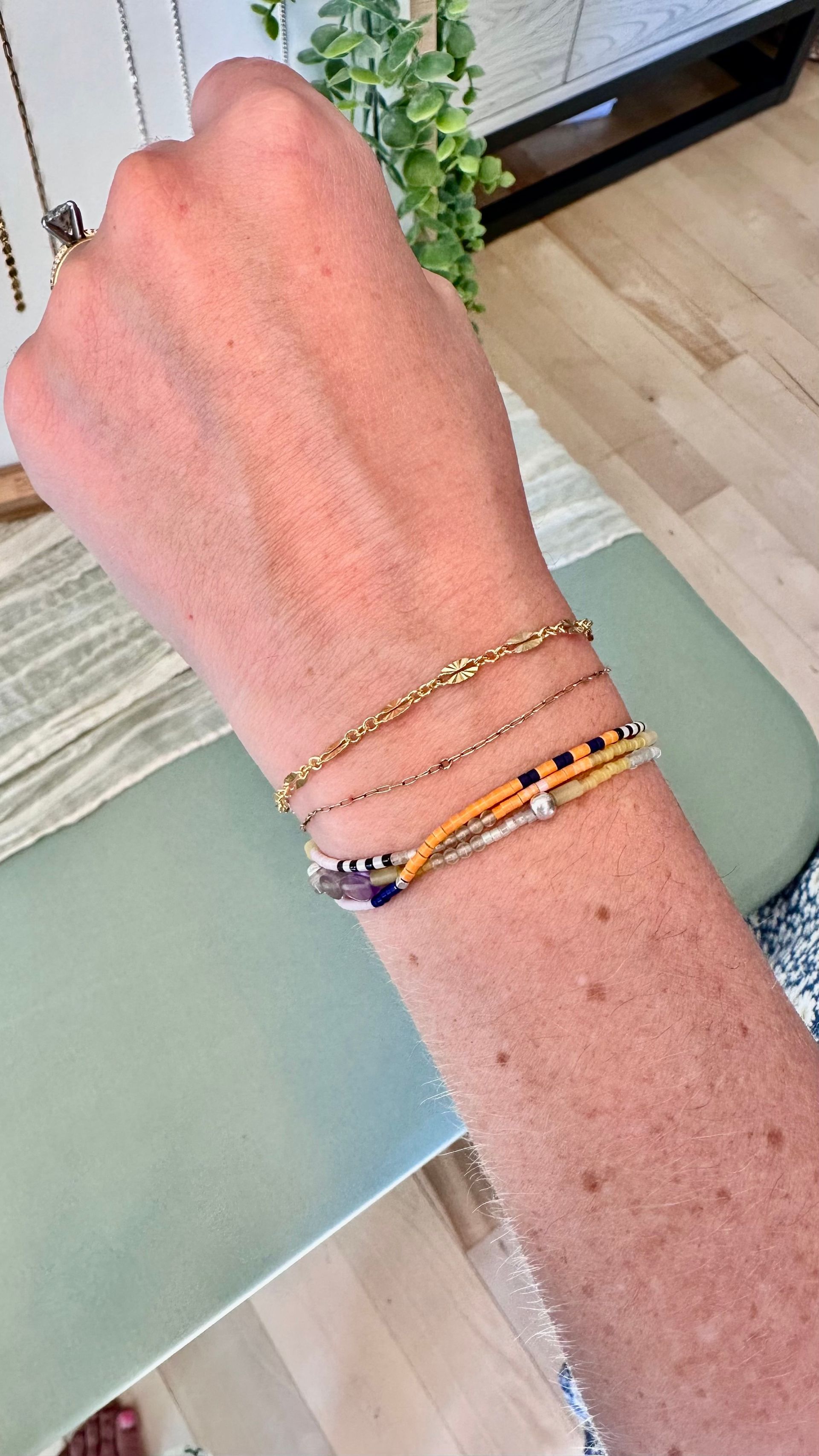 Wrist with stack of gold and colorful beaded bracelets.