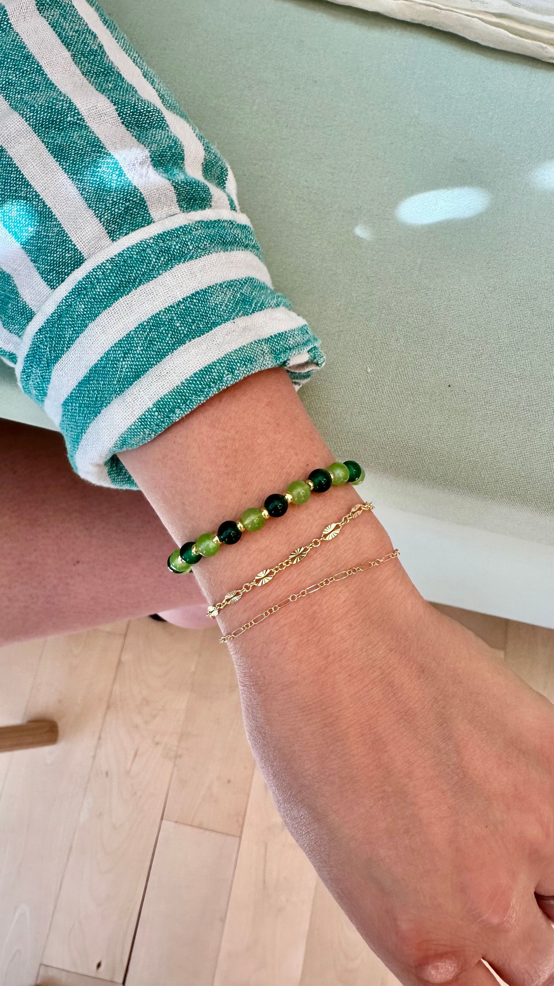 Wrist with three bracelets, green and gold, and a striped green and white sleeve.