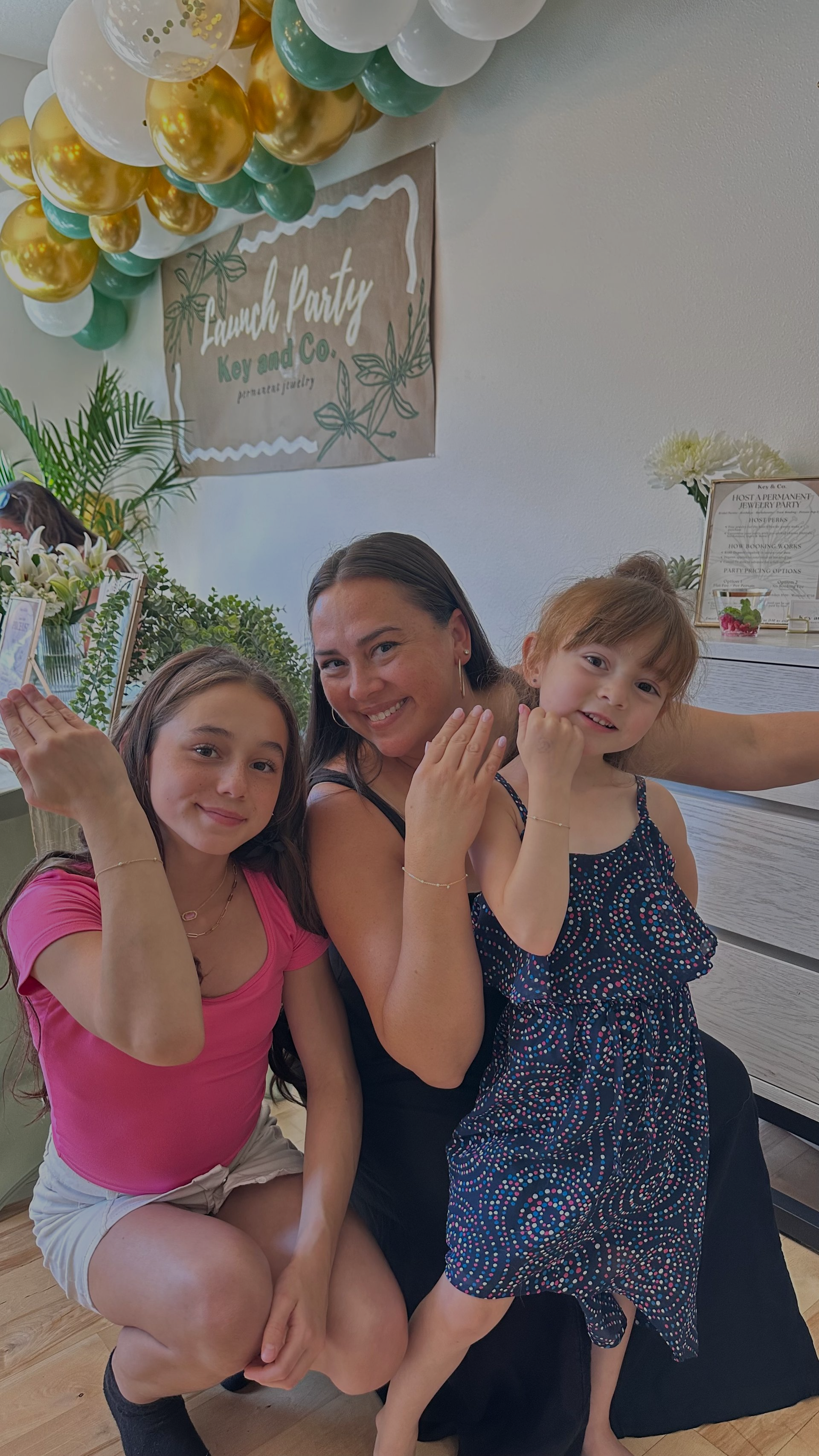 Woman with two children, smiling, with a party backdrop featuring balloons and a sign.
