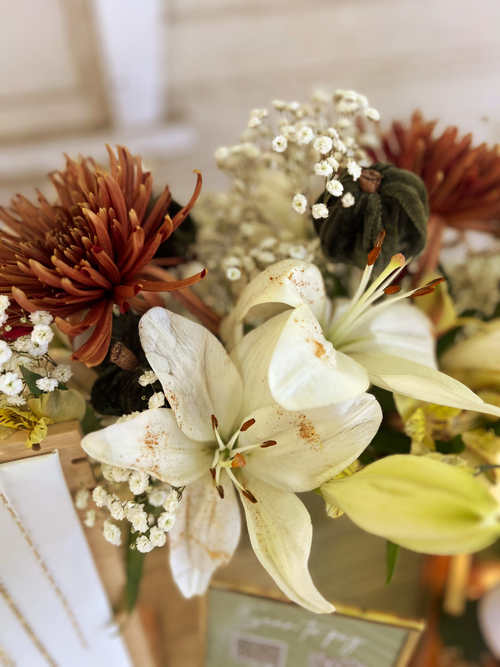 Close-up of a floral arrangement with white lilies, brown chrysanthemums, and baby's breath.