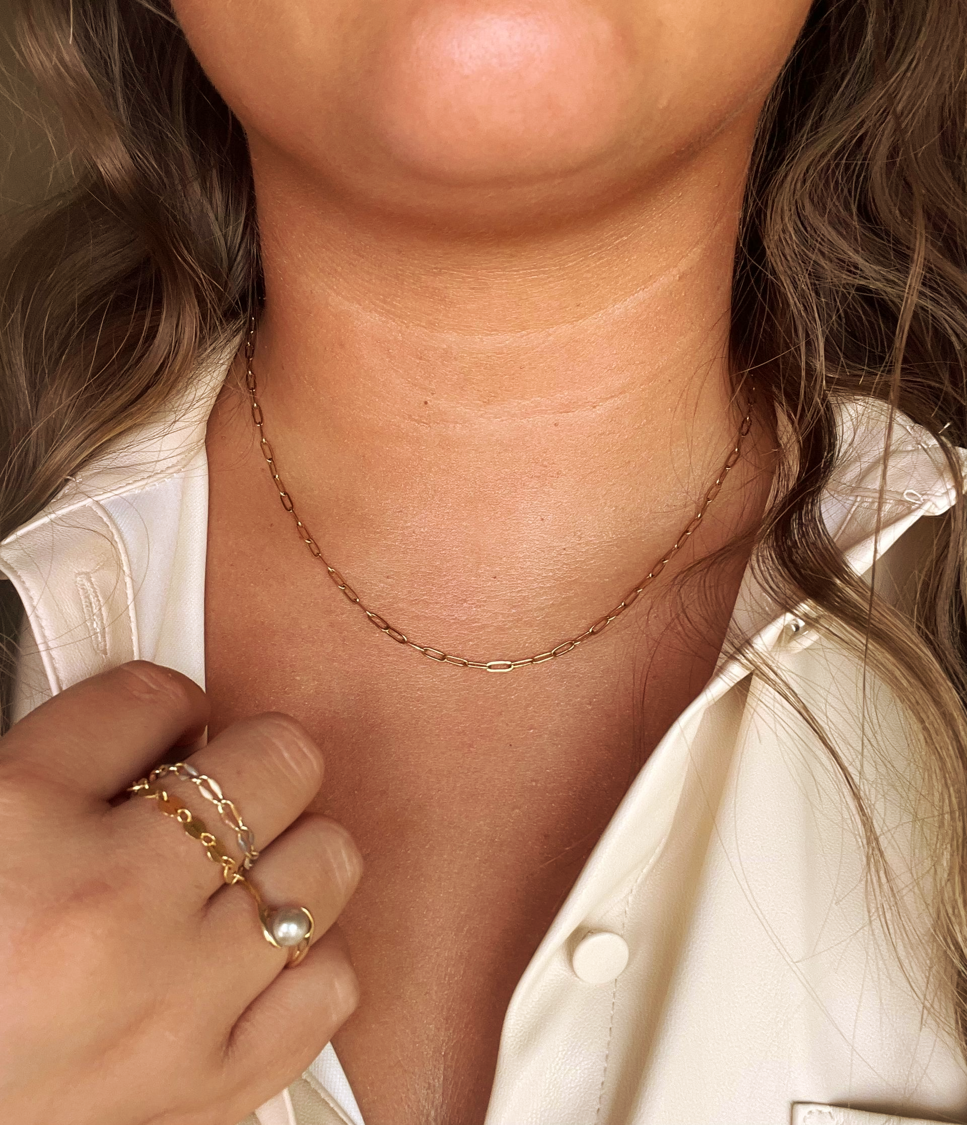 Woman wearing gold necklace and rings, cream shirt; skin shows noticeable discoloration on the neck.