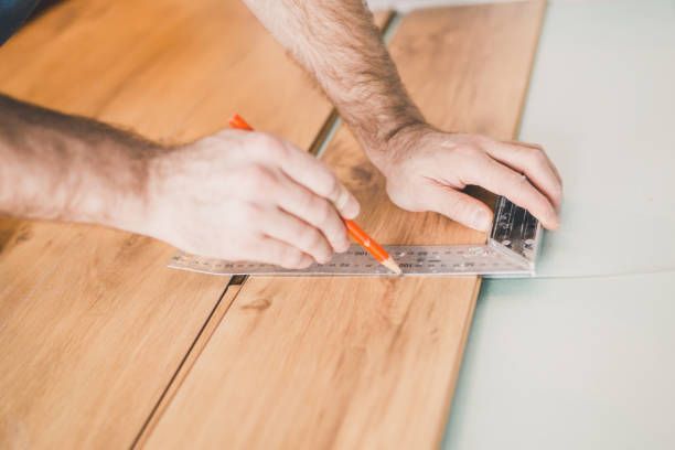 A person using a ruler and pencil to measure and mark vinyl flooring.