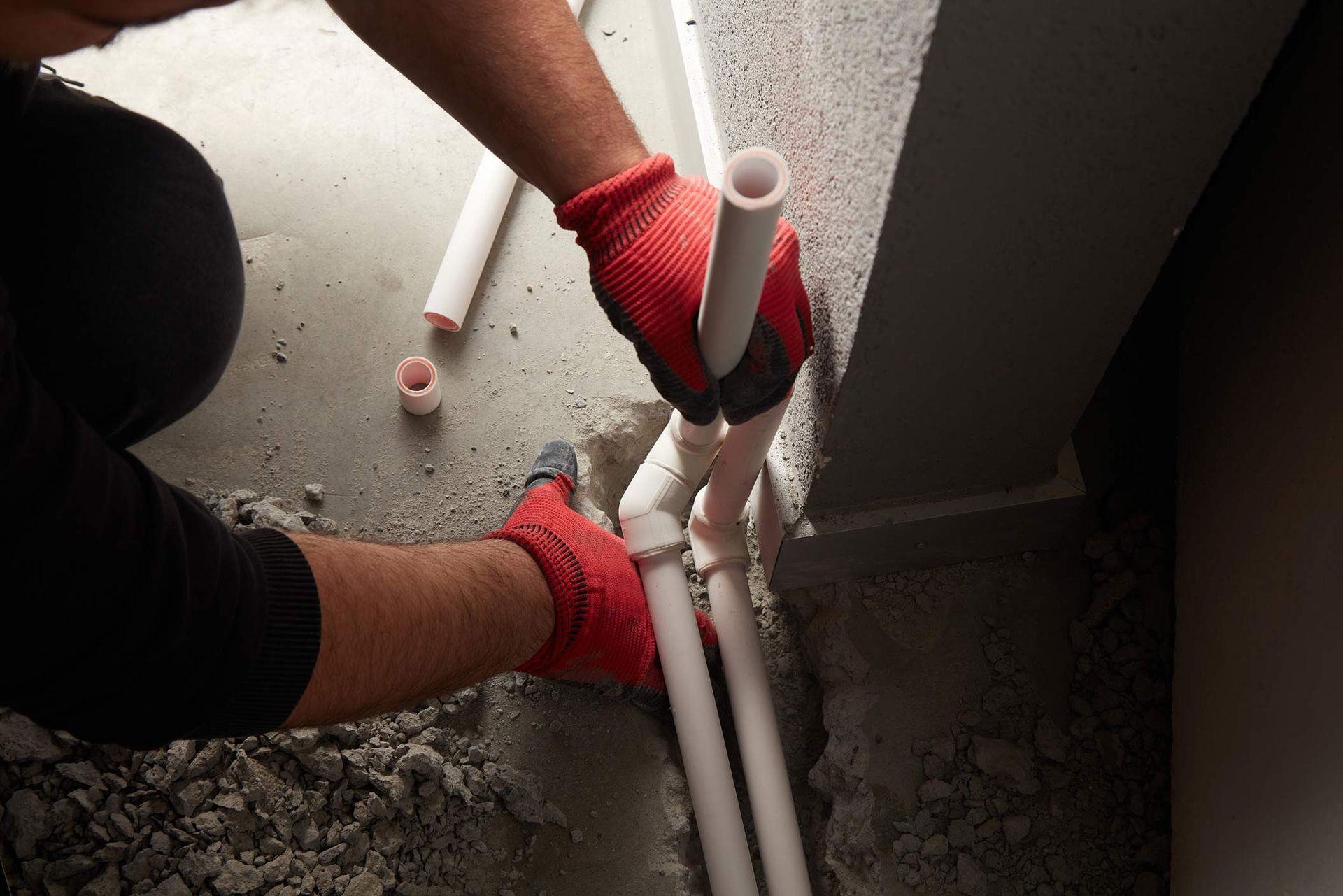 A man wearing red gloves is working on a pipe.