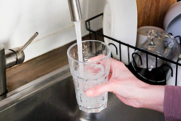 A person is pouring water into a glass in a kitchen sink