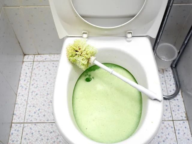 A toilet with green foam and a toilet brush in it